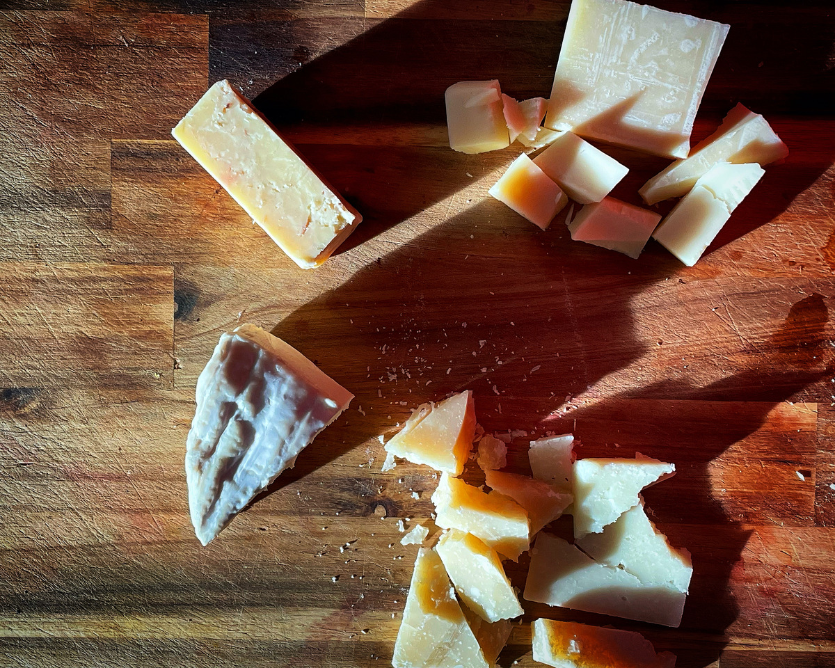 an over head view of cheese leftovers on a wood board casting long shadows